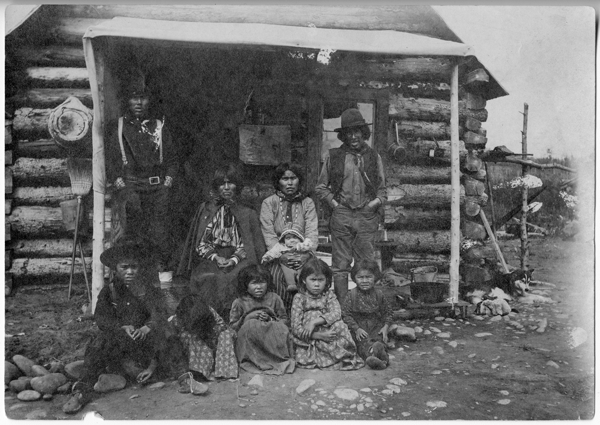 Black and white image of a family posing in front of a log cabin.